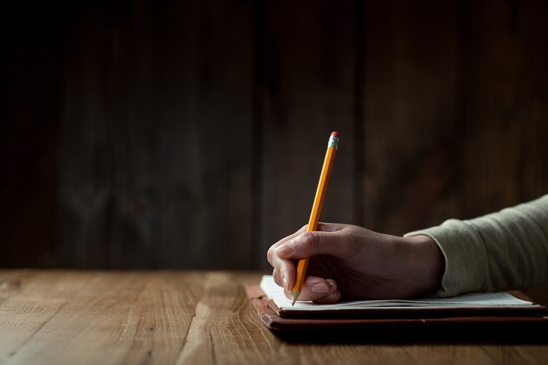 Closeup of woman's hand writing on paper over wooden table
